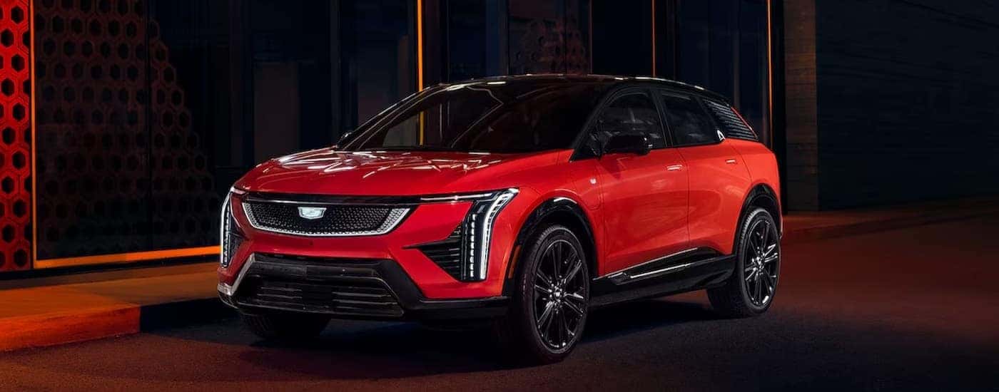 A red and black 2025 Cadillac OPTIQ is shown parked near a city curb.