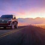 A red 2024 Cadillac Escalade driving through the mountains at sunset.
