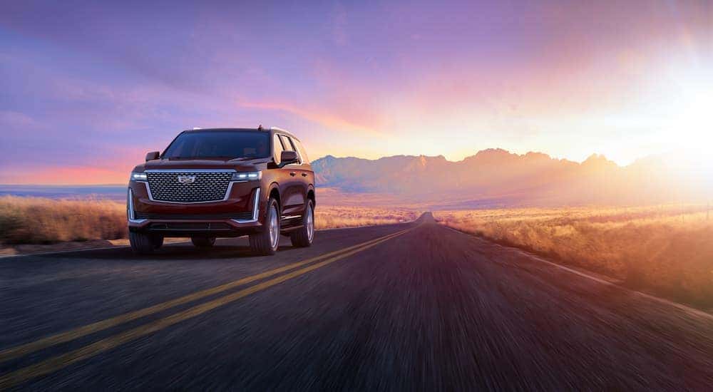 A red 2024 Cadillac Escalade driving through the mountains at sunset.