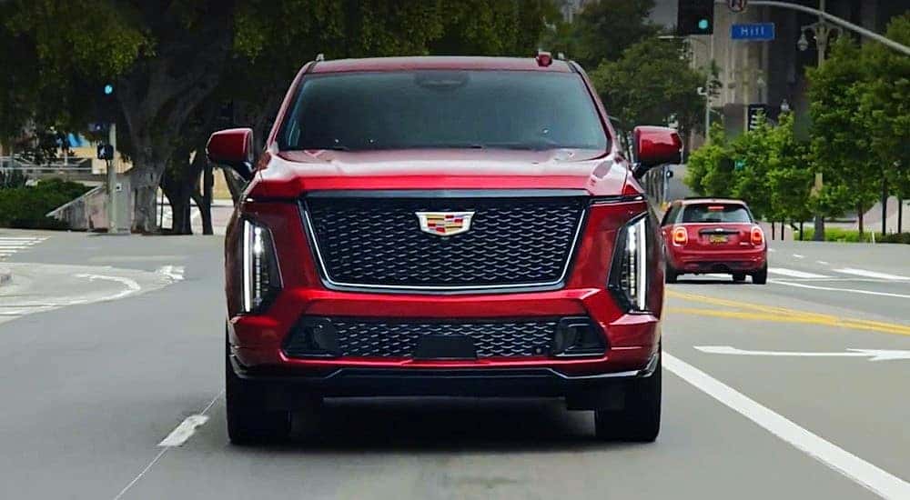 A red 2025 Cadillac Escalade-V is shown driving on a city street.