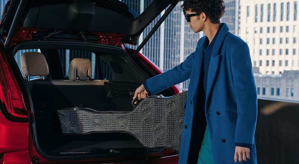 A person putting a guitar case in a red 2025 Cadillac XT4
