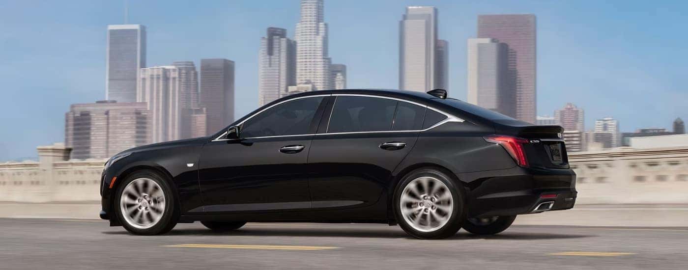 A black 2024 Cadillac CT5 is shown driving on a highway near a city.