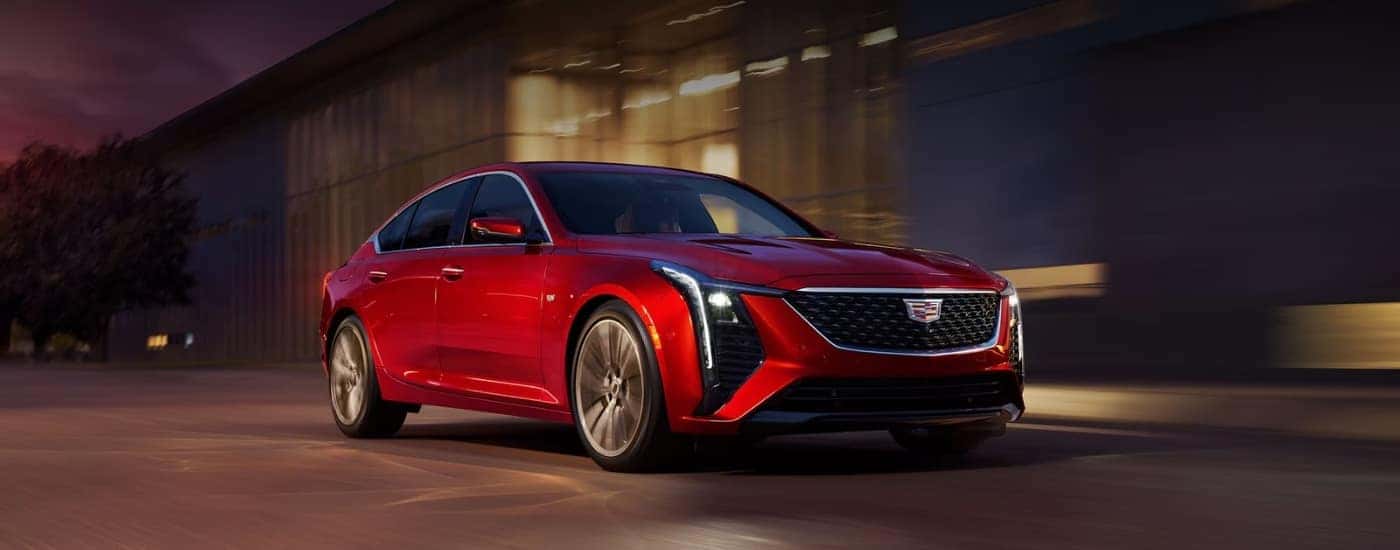 A red 2025 Cadillac CT5 for sale is shown driving on a city street.