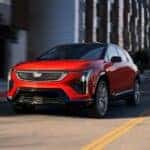 Red 2026 Cadillac OPTIQ-V driving down a road from a dealer with Cadillac EVs for sale.