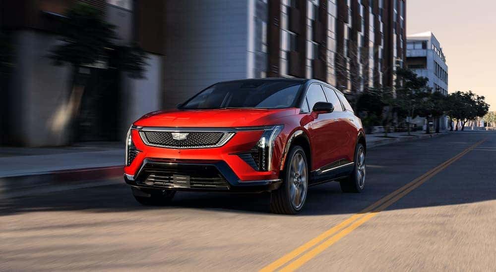 Red 2026 Cadillac OPTIQ-V driving down a road from a dealer with Cadillac EVs for sale.