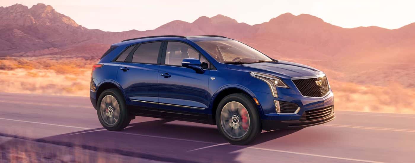 A blue 2026 Cadillac XT5 driving down a mountain-lined road at sunrise.