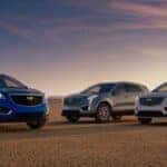A trio of 2026 Cadillac XT5 SUVs, blue, dark gray and light gray, parked during sunset.
