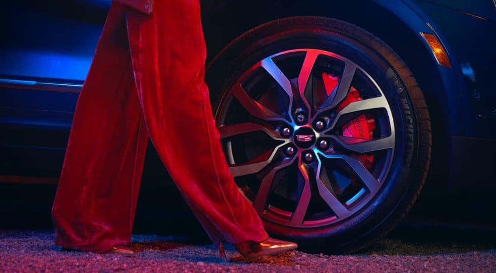 A woman walking by the tire of a dark blue 2026 Cadillac XT5 at night.