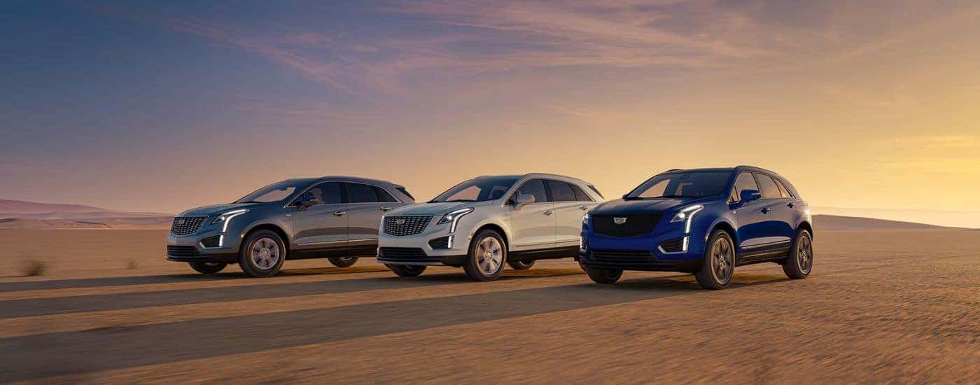 A gray, white and blue 2026 Cadillac XT5 trio parked on a sandy field at sunrise.