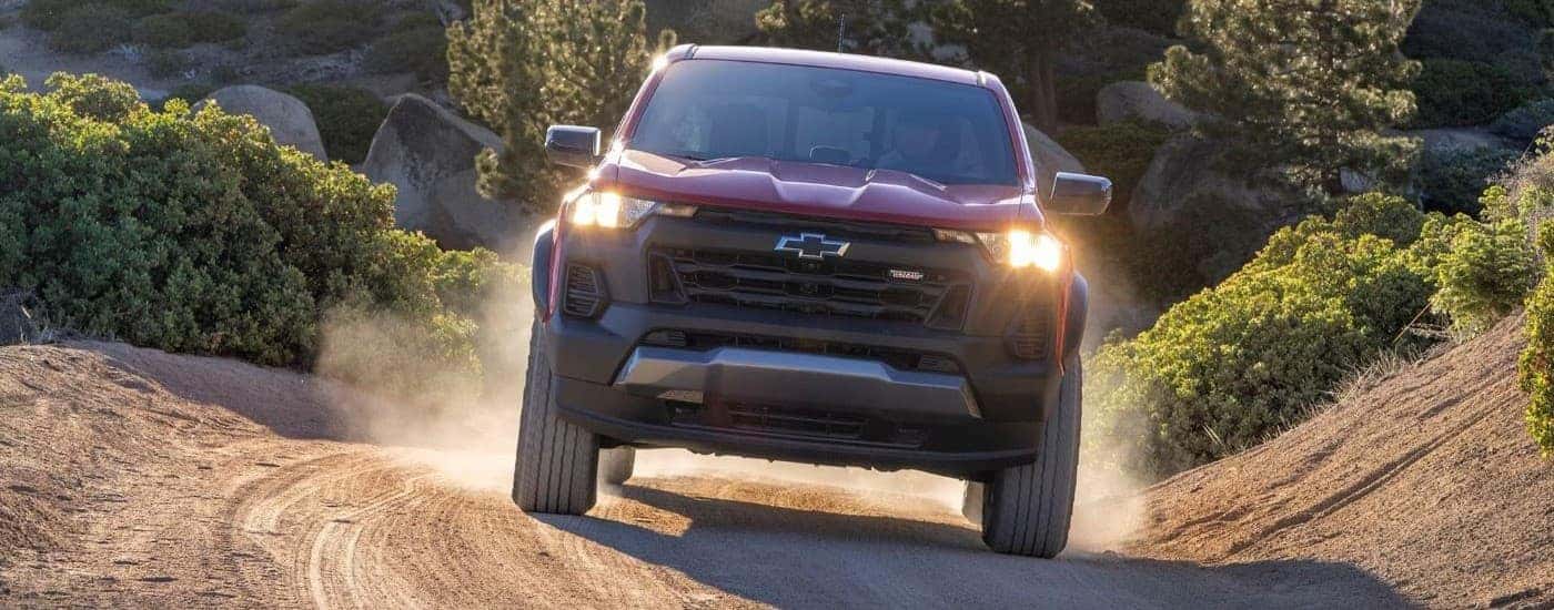 A red 2023 Chevy Colorado Trail Boss is shown from the front on a dusty trail.