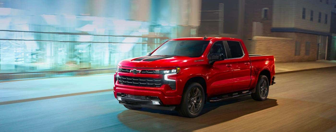 A red 2023 Chevy Silverado 1500 RST is shown from the side driving on a city street.
