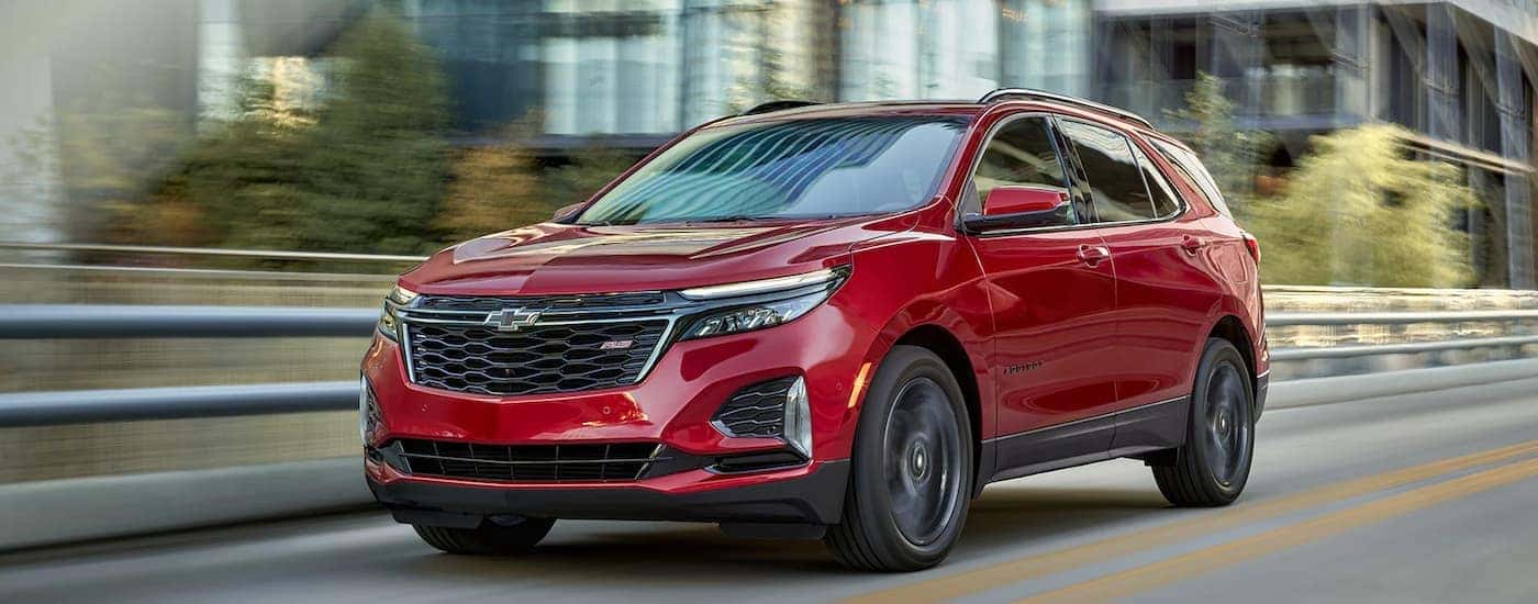 A red 2023 Chevy Equinox RS is shown driving on a highway away from a city.