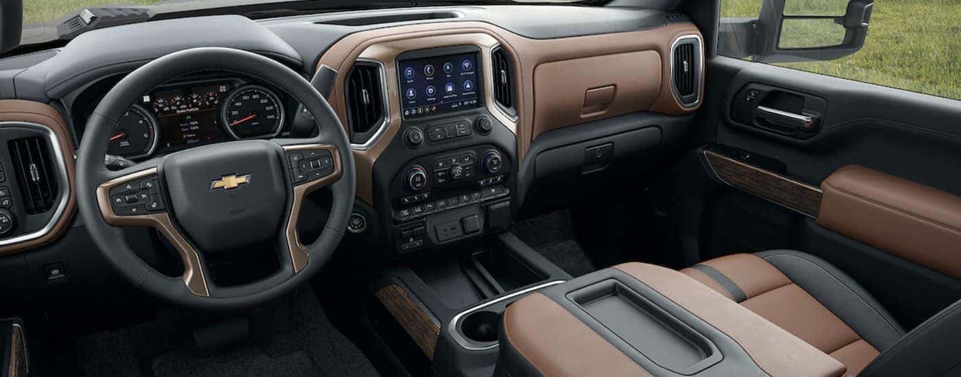 The black and brown interior of a 2023 Chevy Silverado 2500 HD shows the steering wheel and infotainment screen.