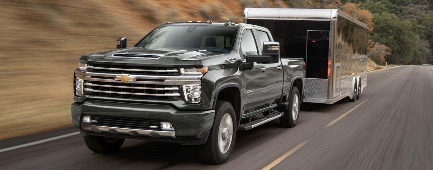 A black 2023 Chevy Silverado 2500 HD is shown towing a trailer on an open road.