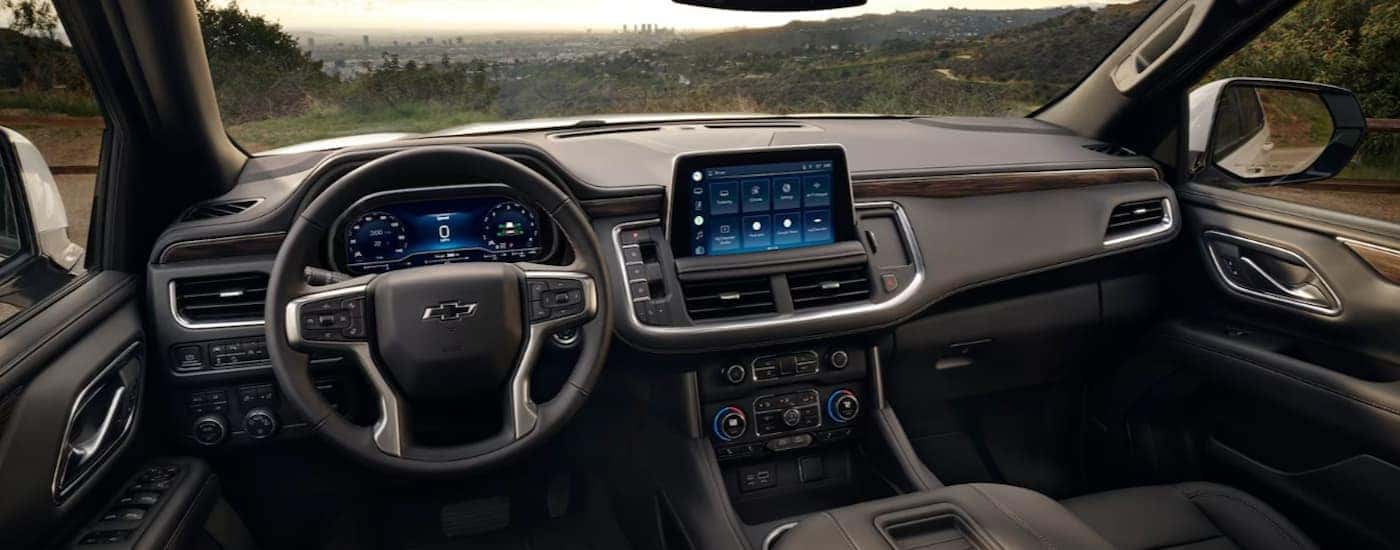 The black interior of a 2023 Chevy Tahoe shows the steering wheel and infotainment.