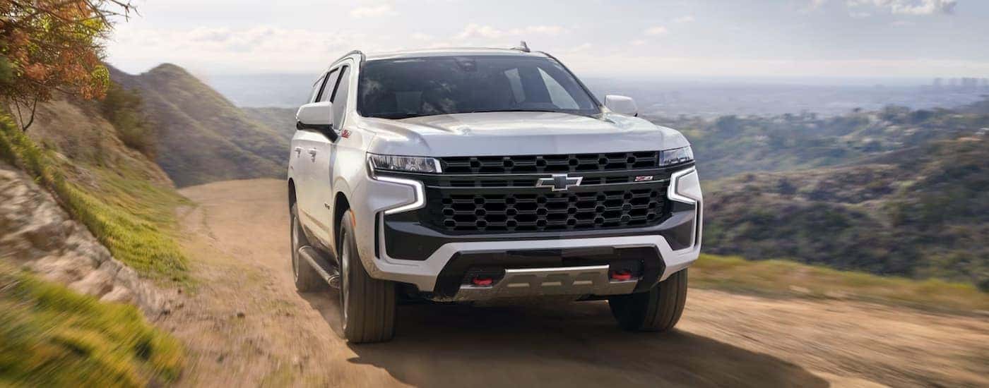 A white 2023 Chevy Tahoe is shown from the front driving on a dirt road.