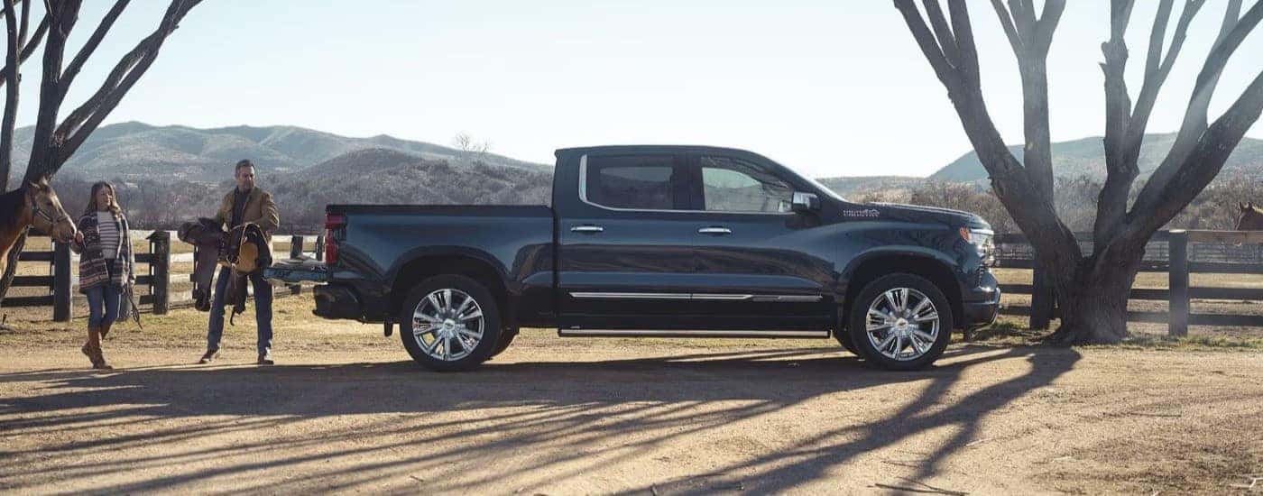 A person is shown loading a saddle into the bed of a blue 2023 Chevy Silverado 1500 High Country.