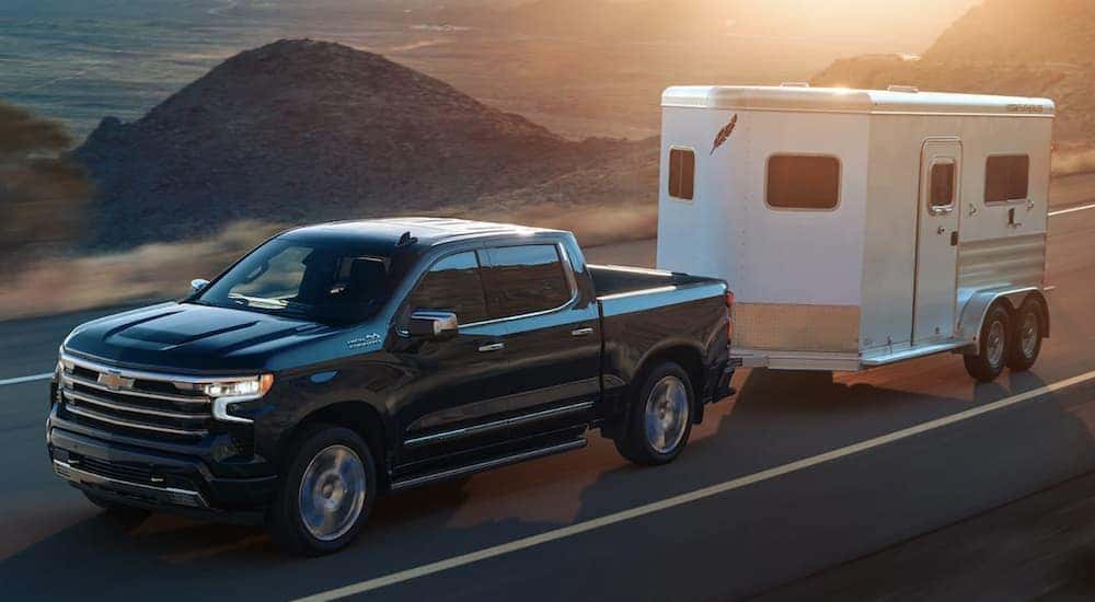 A black 2024 Chevy Silverado 1500 is shown towing a trailer on an open road.