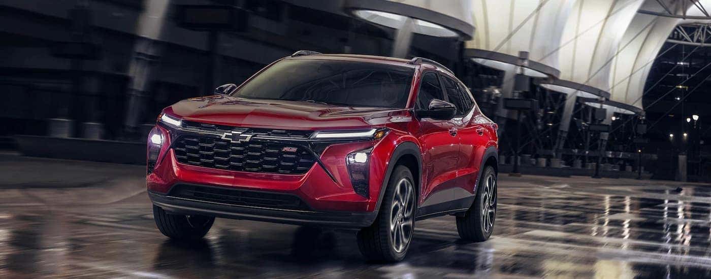 A red 2024 Chevy Trax RS is shown driving on a city street.