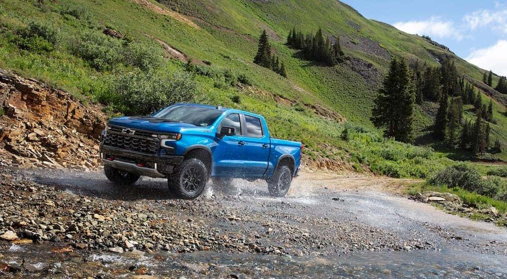 A blue 2024 Chevy Silverado 1500 ZR2 is shown from the front at an angle while driving through a creek after leaving a Chevy Silverado dealer.