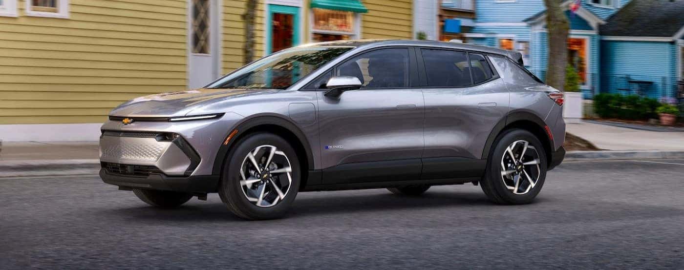 A silver 2024 Chevy Equinox EV is shown driving near a shop.