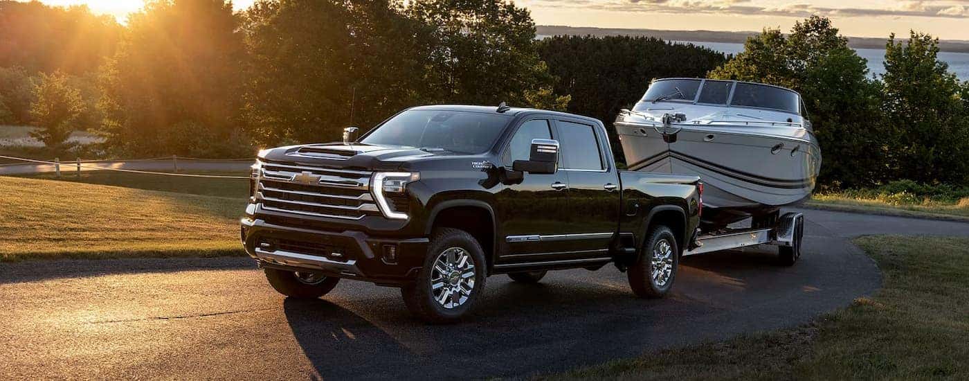 A black 2024 Chevy Silverado 2500 HD High Country is shown towing a boat on a winding road.