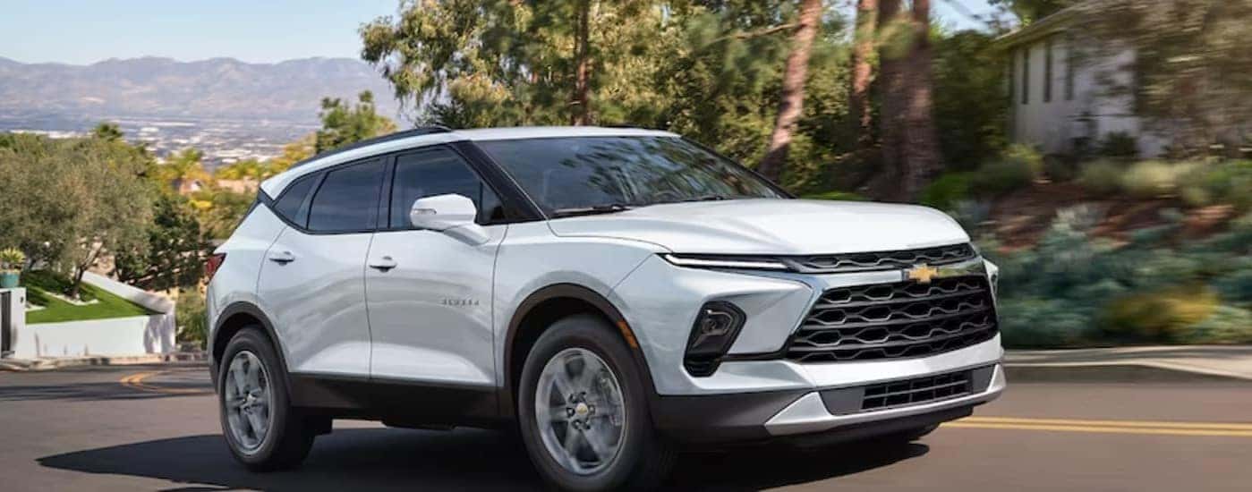 A white 2024 Chevy Blazer is shown driving on a city street.