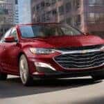 A red 2024 Chevy Malibu driving on a bridge in the city.