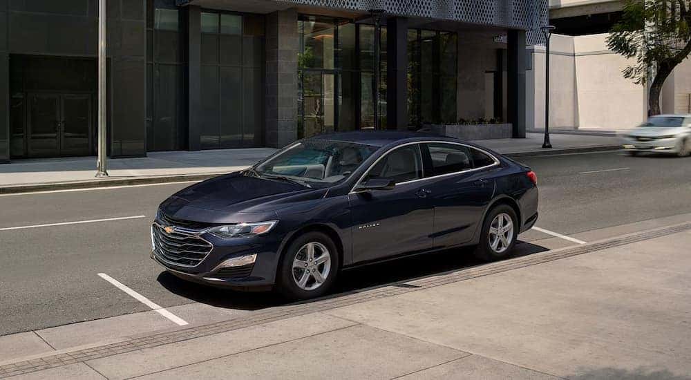 A dark blue 2024 Chevy Malibu in a parallel parking space in the city.