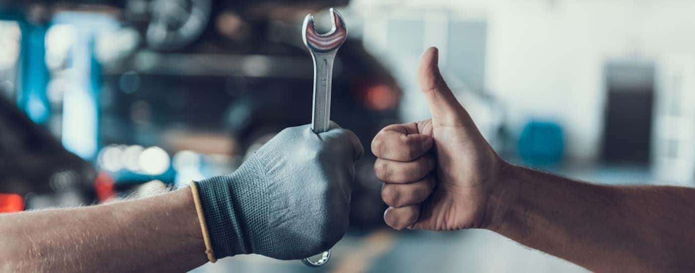 A hand is shown giving a thumbs up next to another hand holding a wrench.