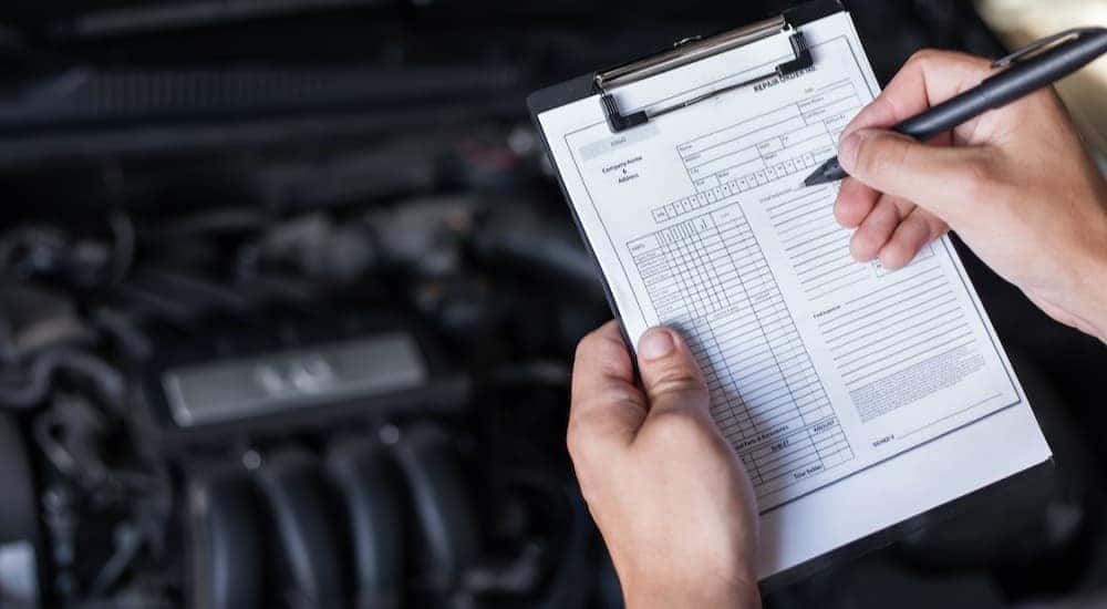 A mechanic is shown holding a clipboard near an engine.