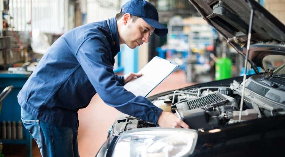 A mechanic is shown inspecting under the hood of a vehicle while performing an auto service.