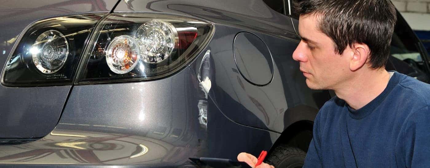 A mechanicis shown looking at a dent on a vehicle.