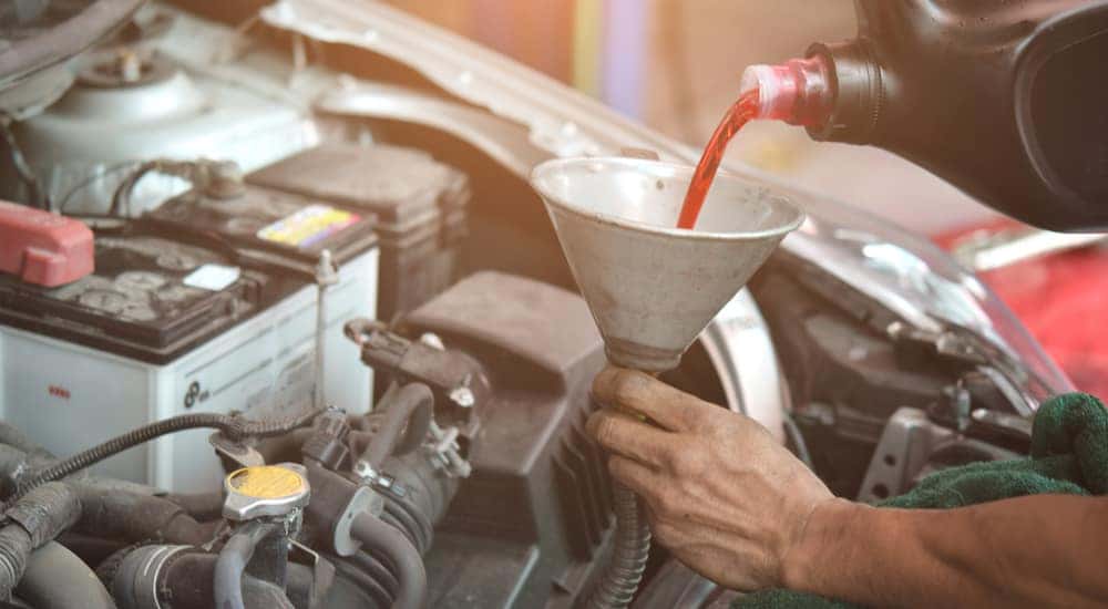 A mechanic is shown pouring transmission fluid through a funnel.