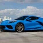 A blue 2024 Chevy Corvette Stingray is shown driving near a city.