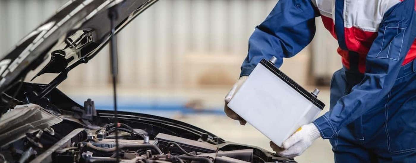 A mechanic is shown holding a car battery.