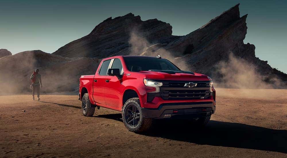 A rock climber walking toward a red 2024 Chevy Silverado 1500 LT Trail Boss parked off-road.