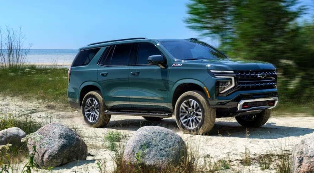 A green 2025 Chevy Tahoe Z71 is shown driving on sand.