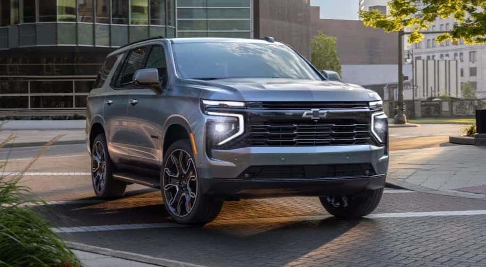 A silver 2025 Chevy Tahoe is shown driving on a city street.