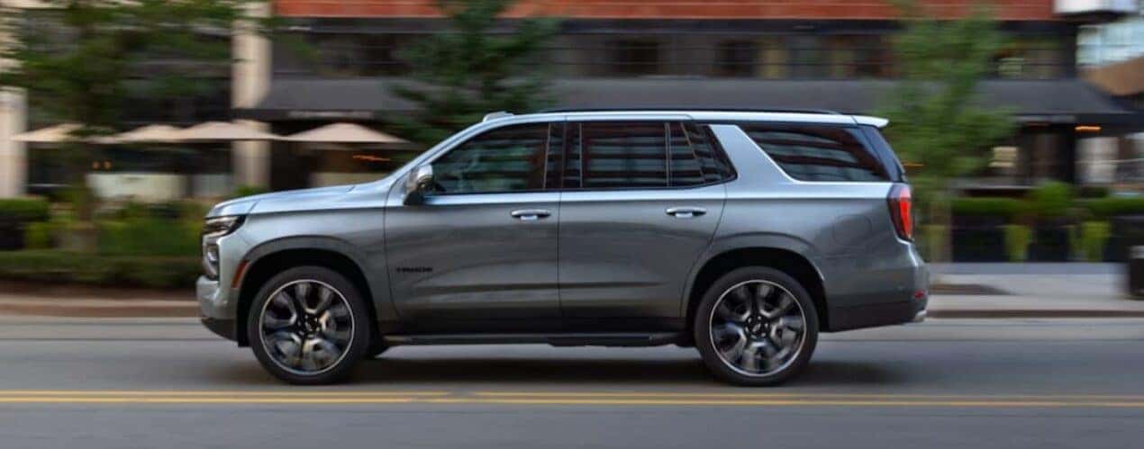 A silver 2025 Chevy Tahoe is shown driving on a city street.