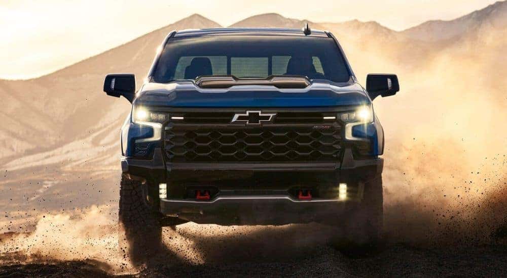 A blue 2024 Chevy Silverado 1500 ZR2 is shown kicking up dust off-road.