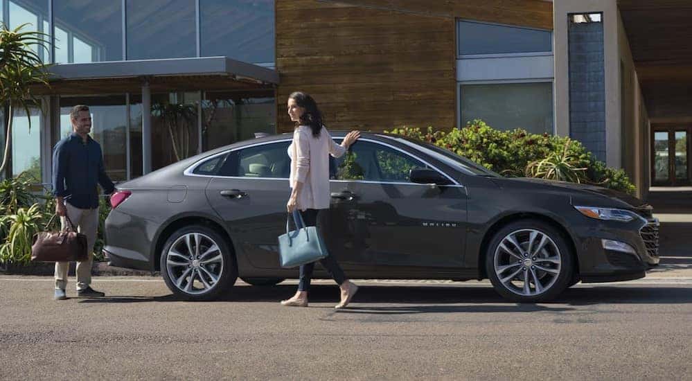 A gray 2025 Chevy Malibu is shown parked near a house.