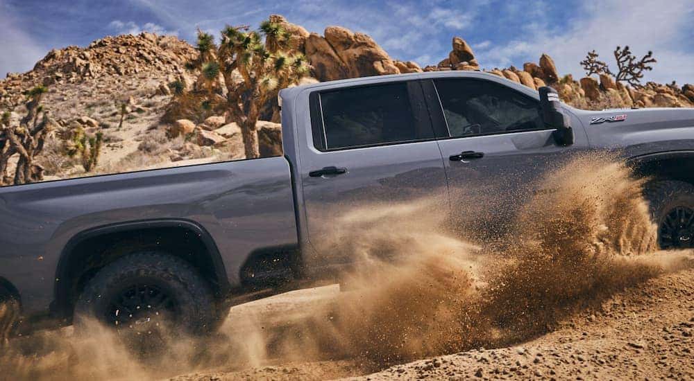 The side of a grey 2025 Chevy Silverado 2500 HD ZR2 off-roading and kicking up sand.