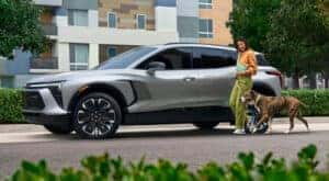 A person is shown walking a dog near a grey 2024 Chevy Blazer EV RS.