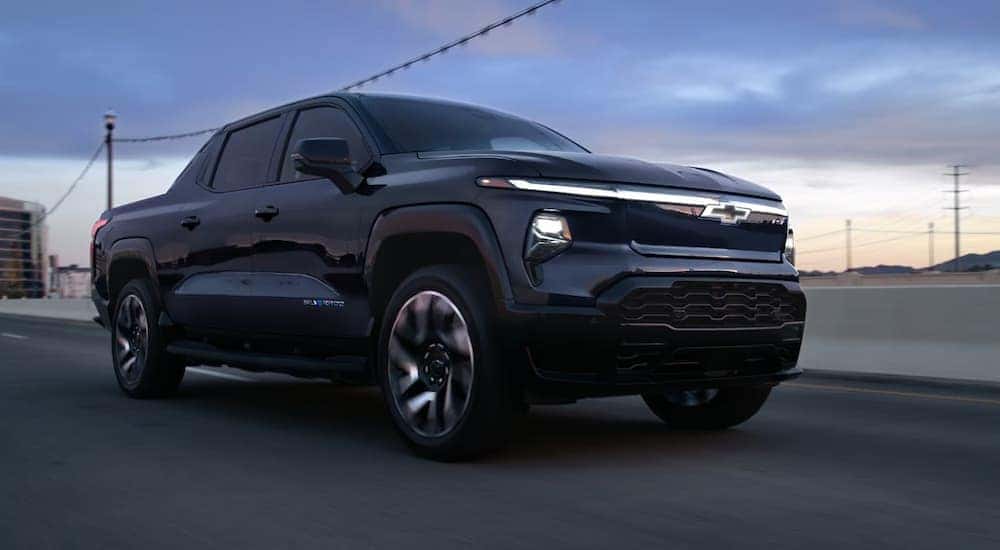 Right angled view of a black 2025 Chevy Silverado EV driving down a road.