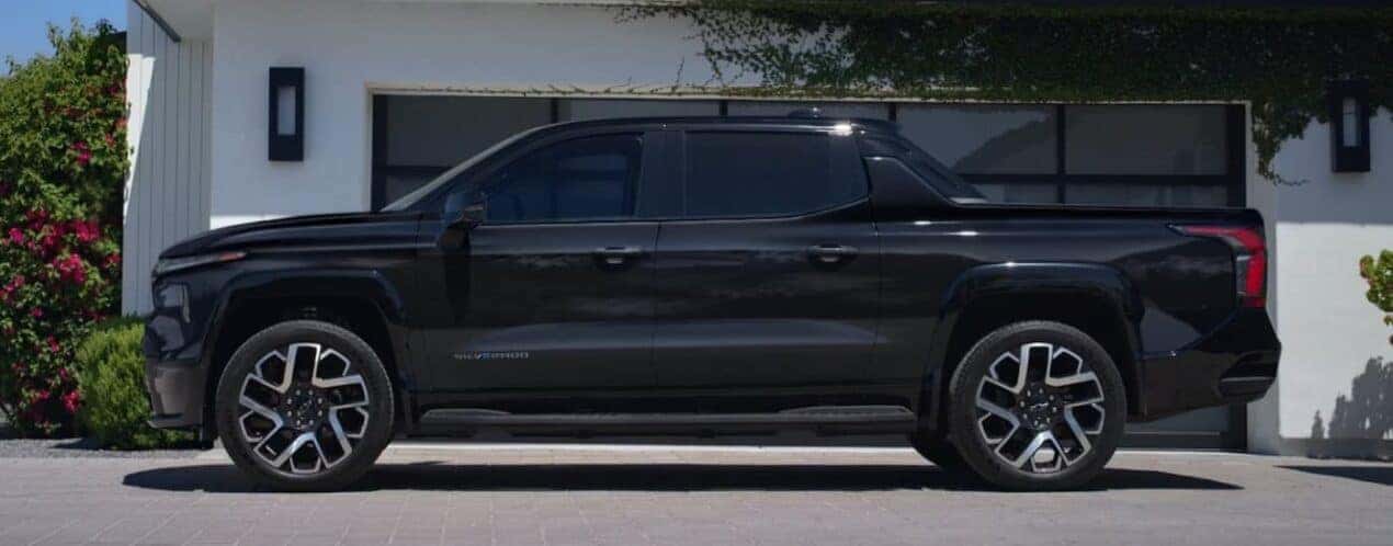 A black 2025 Chevy Silverado EV is shown parked near a garage.