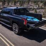 Rear overhead view of a black 2024 Chevy Silverado EV driving with a kayak in the bed.