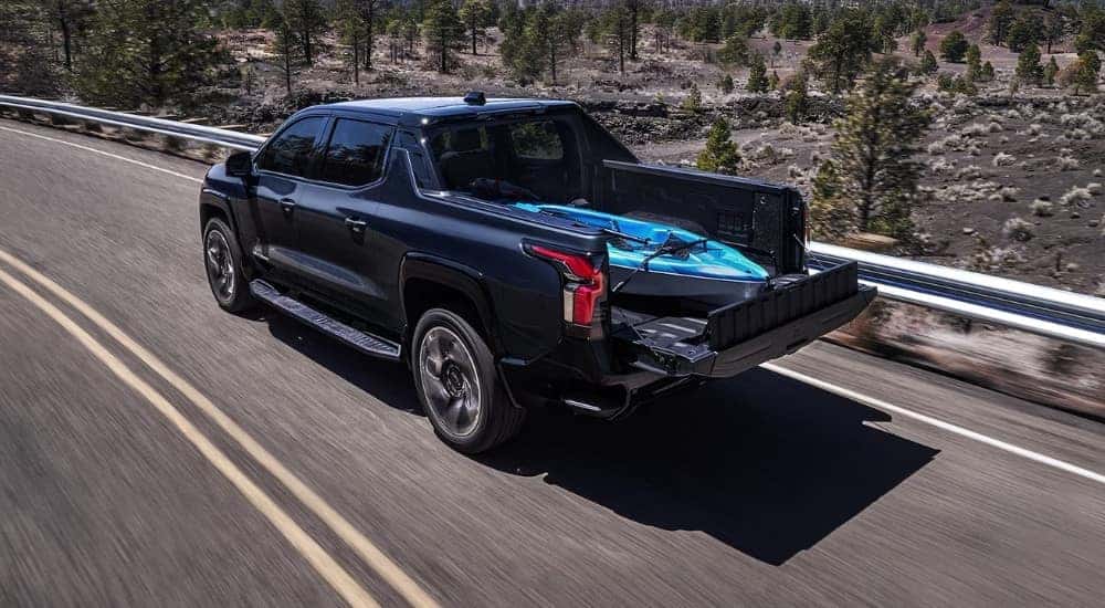 Rear overhead view of a black 2024 Chevy Silverado EV driving with a kayak in the bed.