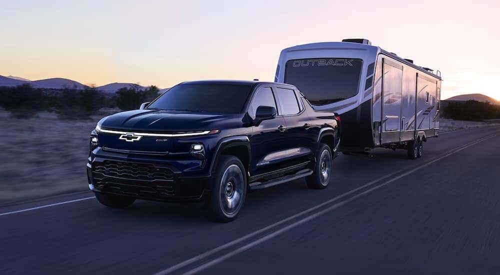 A black 2024 Chevy Silverado EV RST towing a camper at dusk.