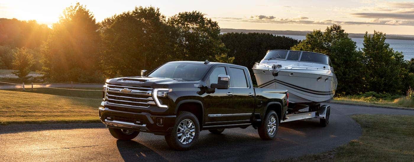 A black 2024 Chevy Silverado 2500 HD High Country is shown from the front at an angle while towing a…